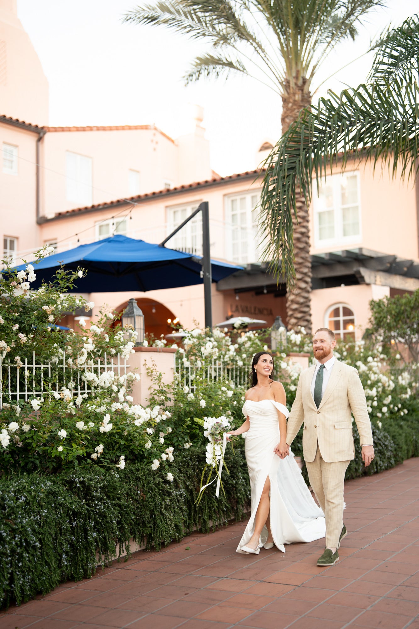 Bride and groom walking down brick sidewalk holding hands