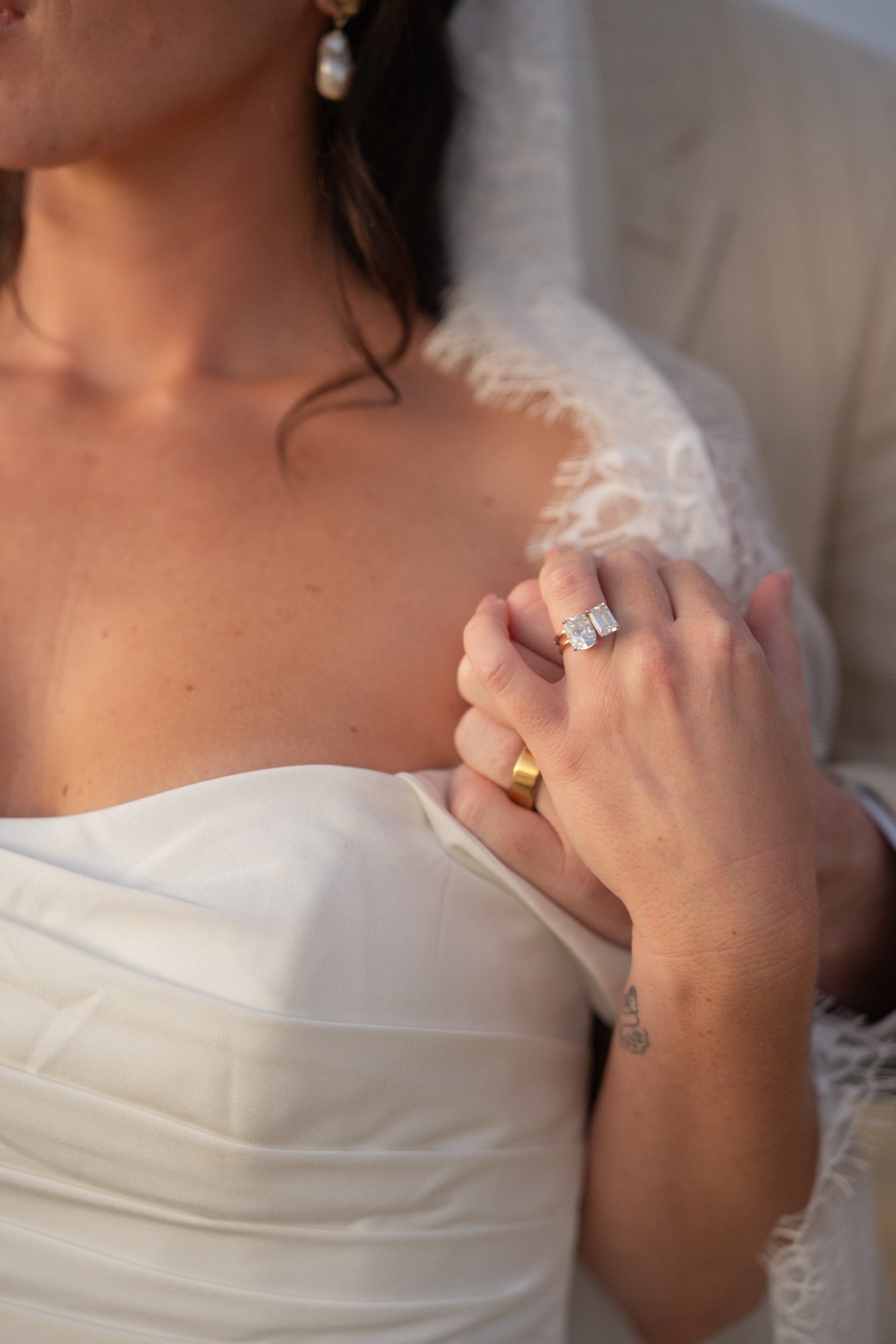 Bride holding groom's hand on her shoulder with wedding rings showing