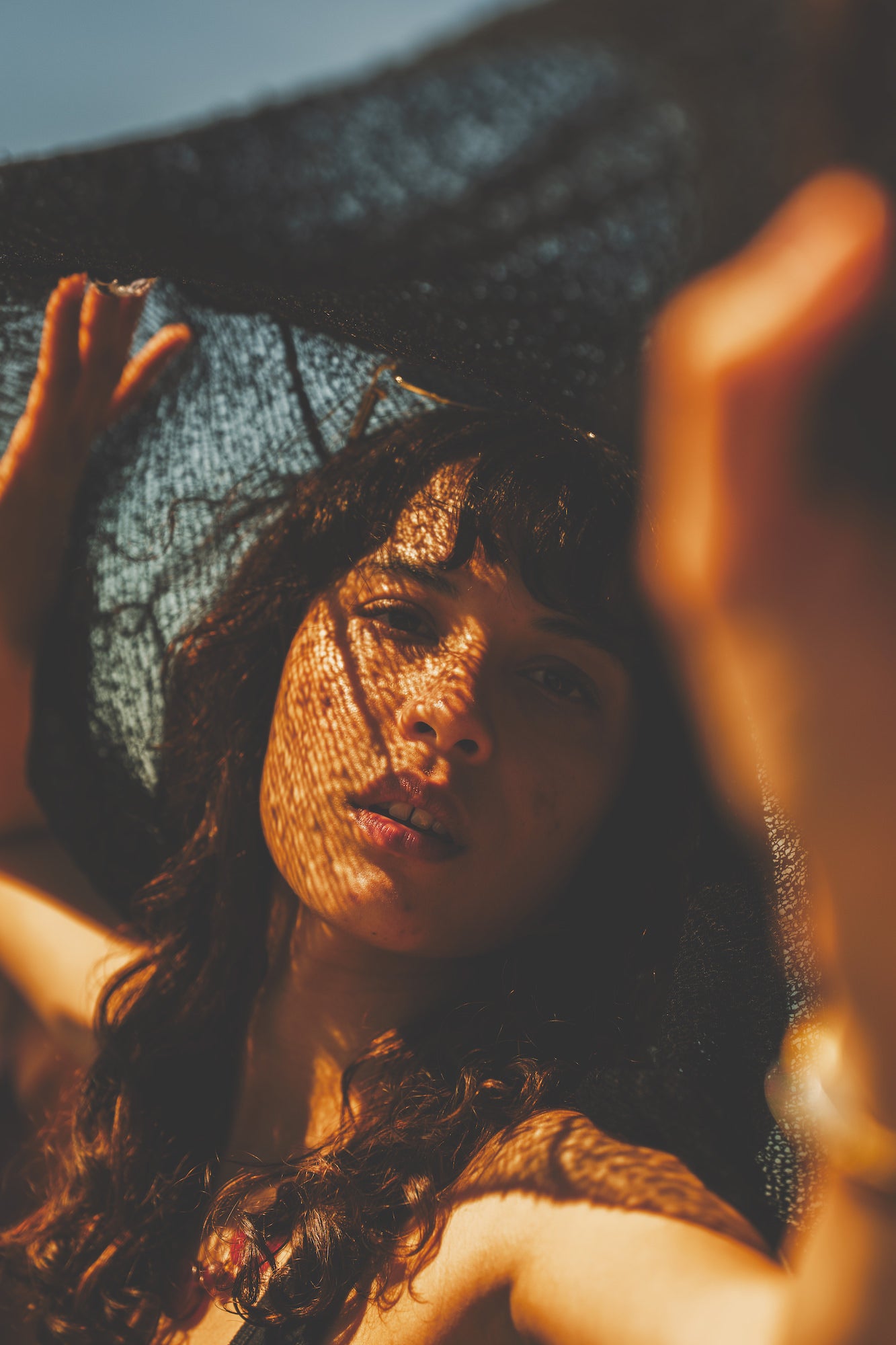 Artistic close‑up portrait with dappled mesh shadows across the face in warm sunset light, coastal editorial style. Artistic close‑up portrait with dappled mesh shadows across the face in warm sunset light, coastal editorial style.