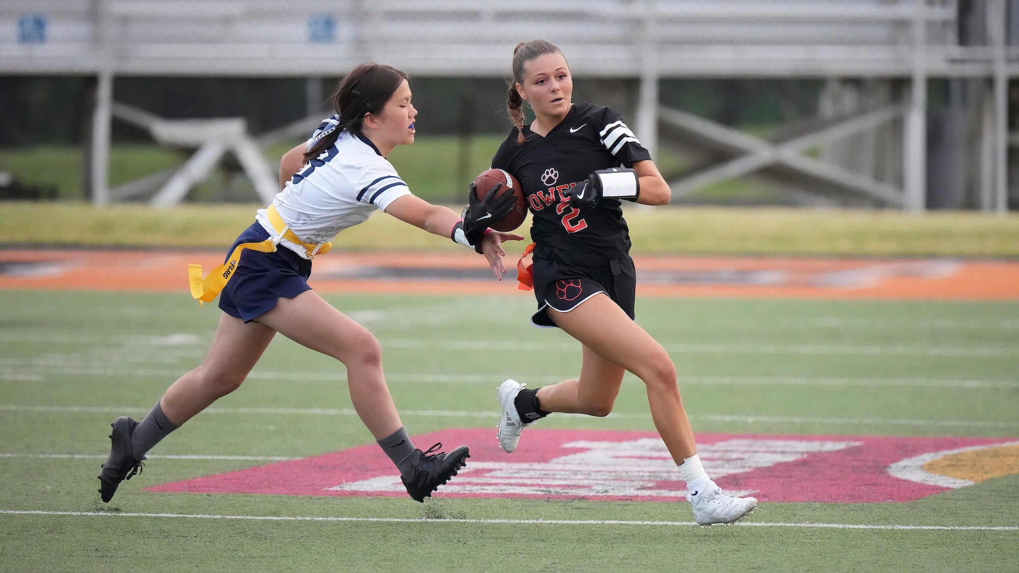 Two girls flag football players run after each other.