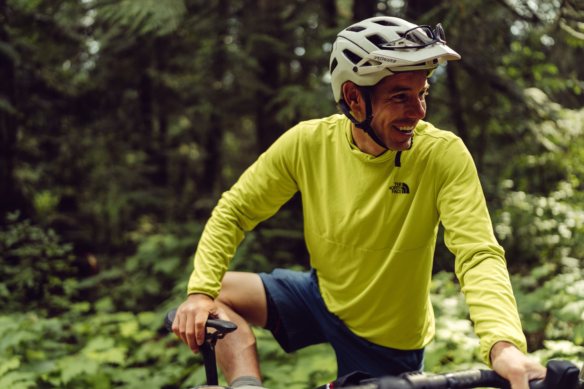 Alex Honnold with his bike in front of a green forest.