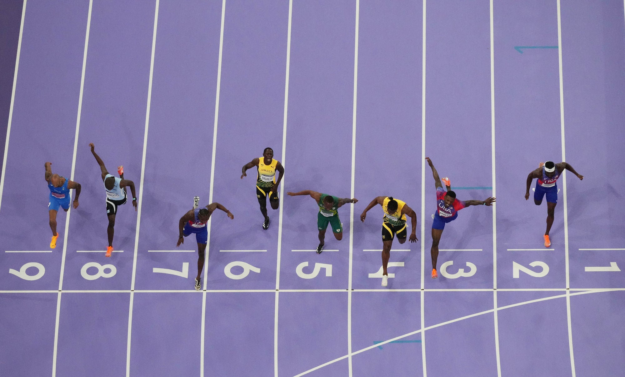 Aerial photo finish of a 100m race, runners crossing a purple track&rsquo;s line.
