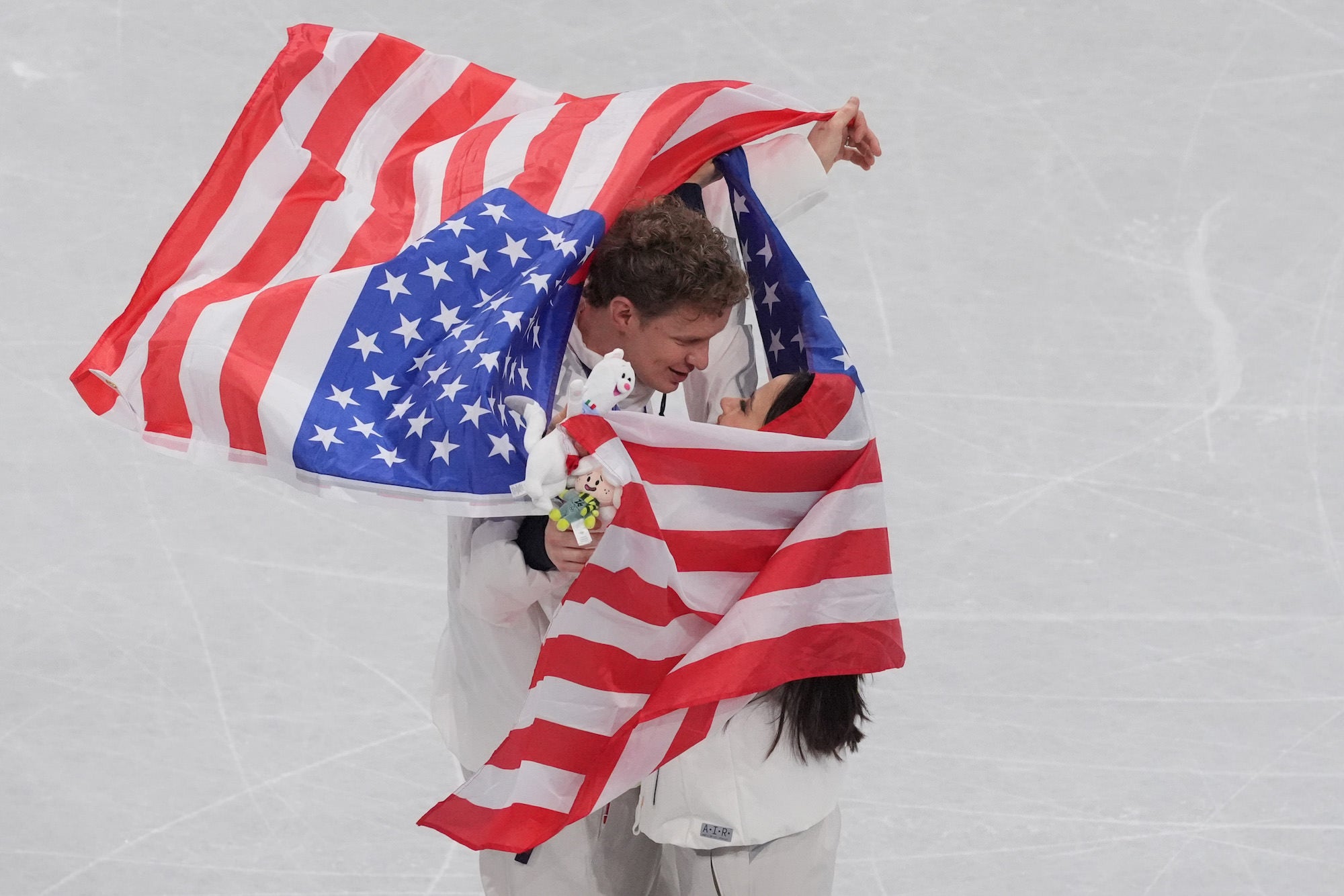 Figure skating pair wrapped in an American flag celebrating on the ice.