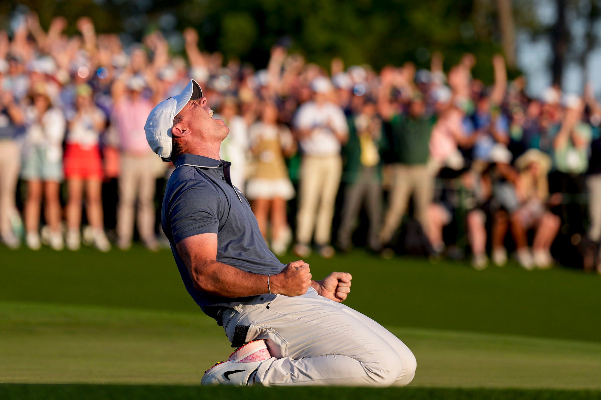 Golfer kneels on the green, fists clenched, roaring as the crowd erupts.