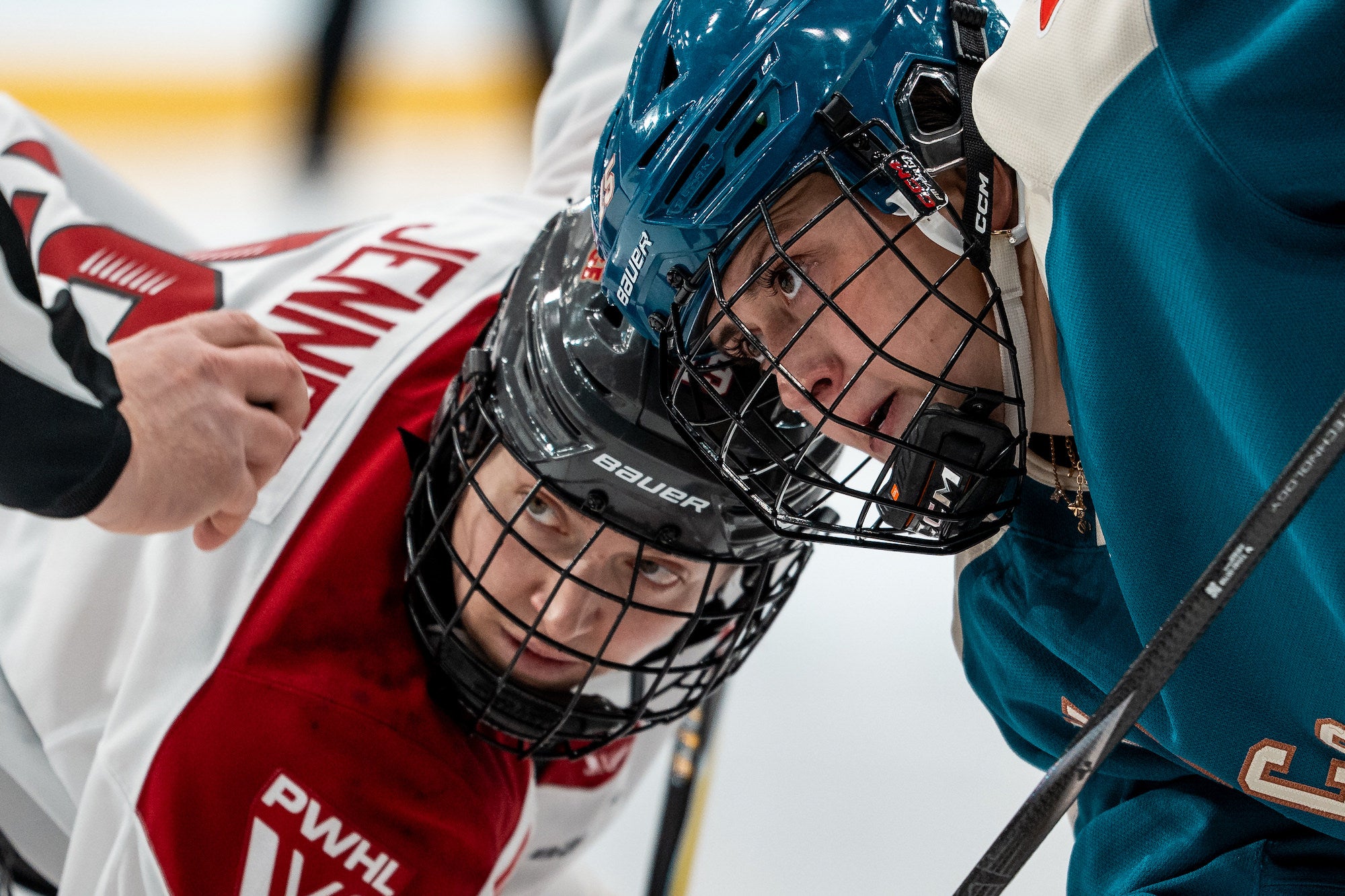 Extreme close-up of two centers leaning in for a faceoff, eyes locked as the official prepares to drop the puck.