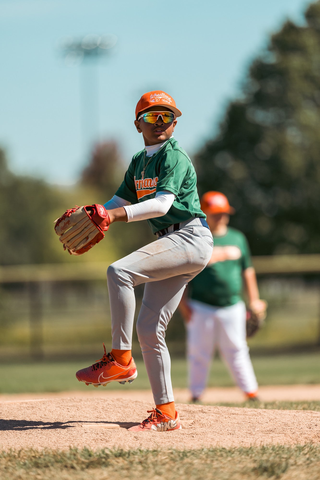 Youth pitcher at peak leg lift, set to deliver from the mound on a sunny spring day.