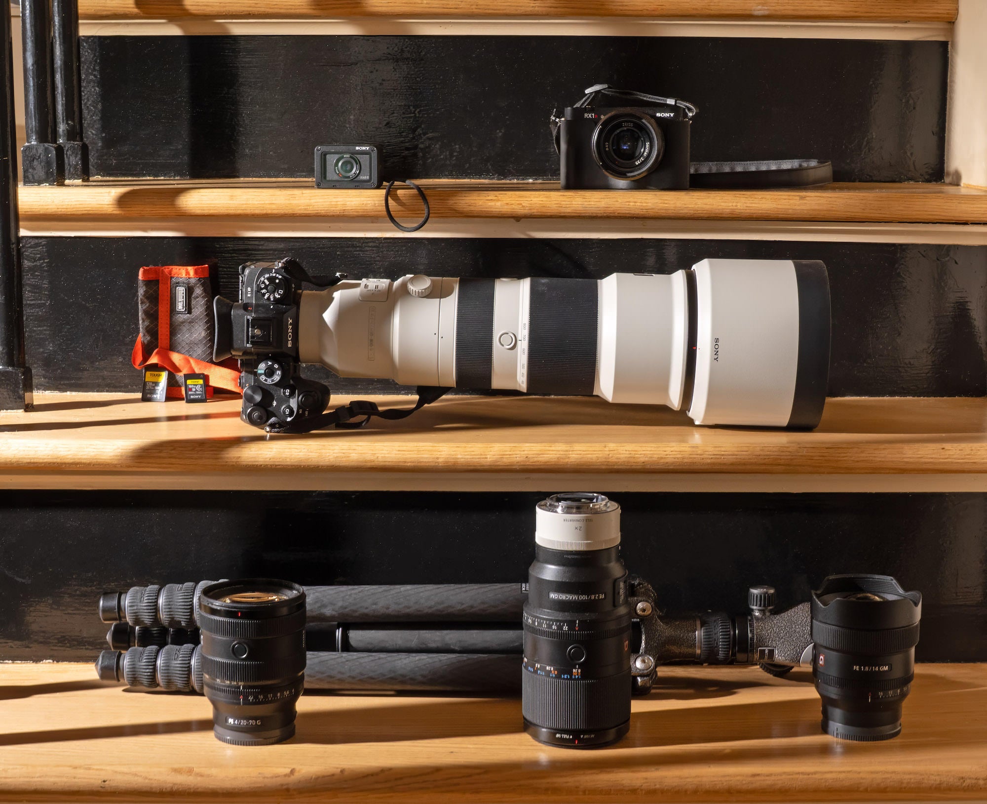 Photo kit on stairs: telephoto zoom on camera, primes, memory cards, and tripod.