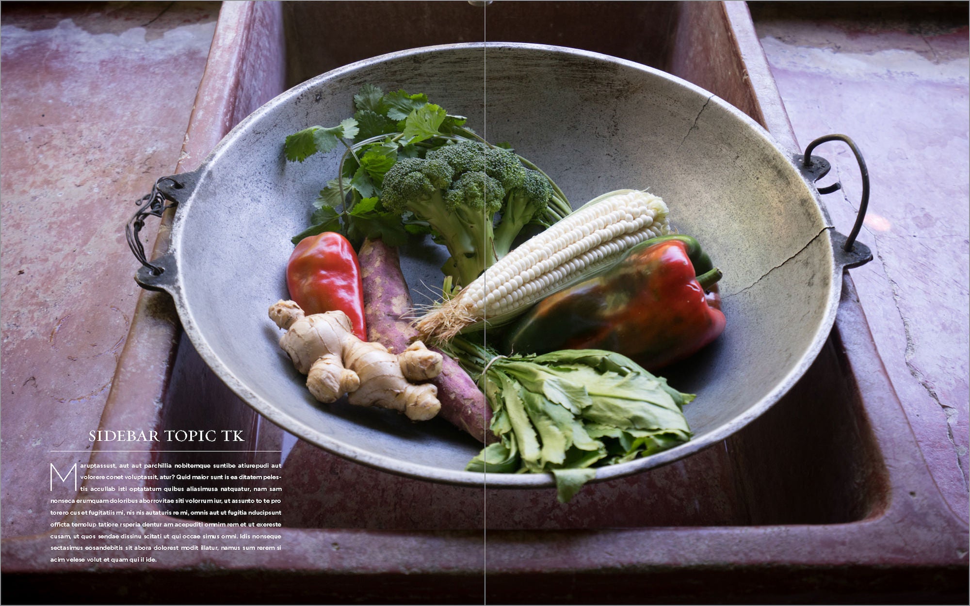 Assorted fresh vegetables&mdash;corn, peppers, broccoli, ginger, herbs&mdash;arranged in a large metal bowl.