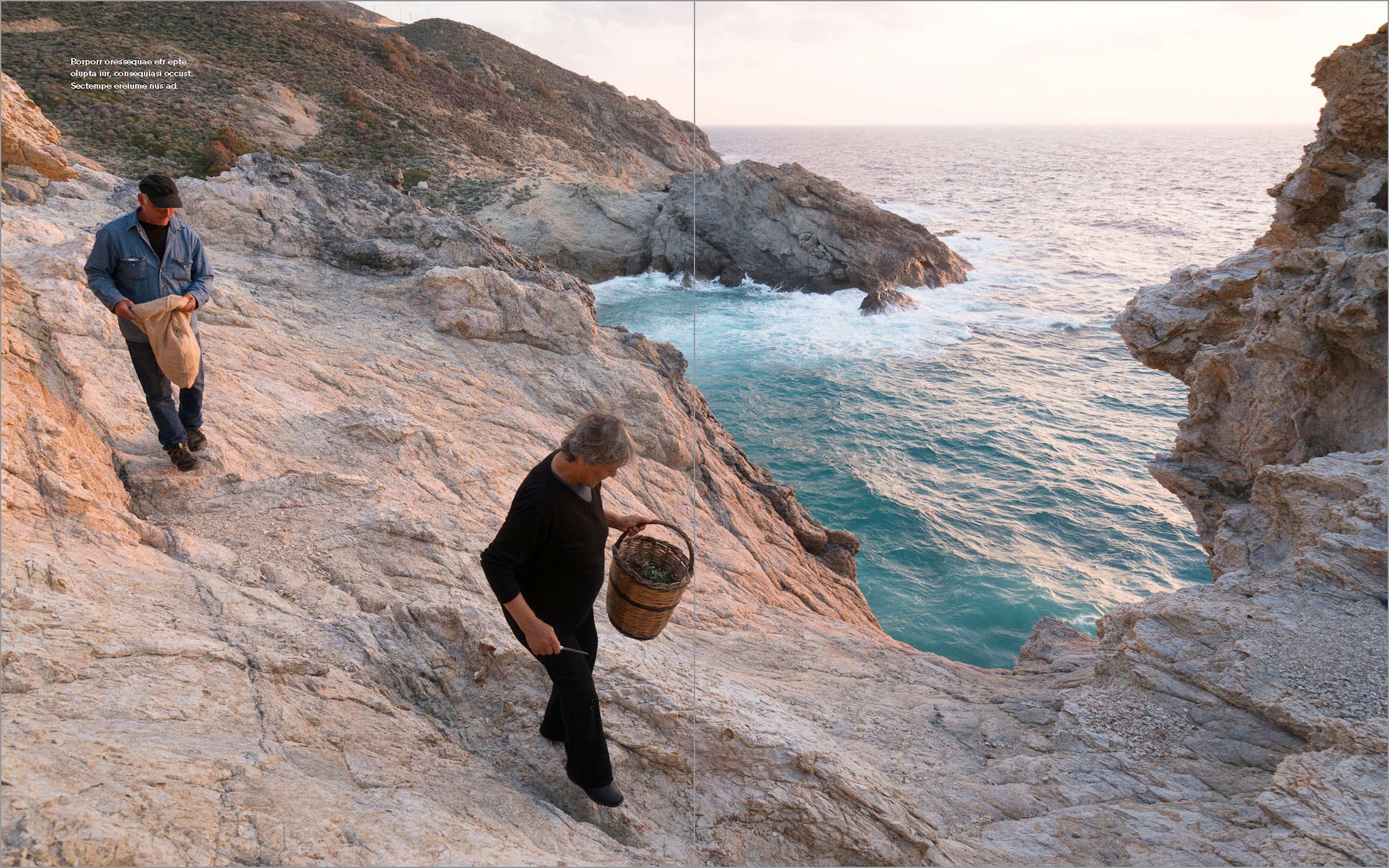 Two people walk along rocky seaside cliffs above turquoise waves at sunset.