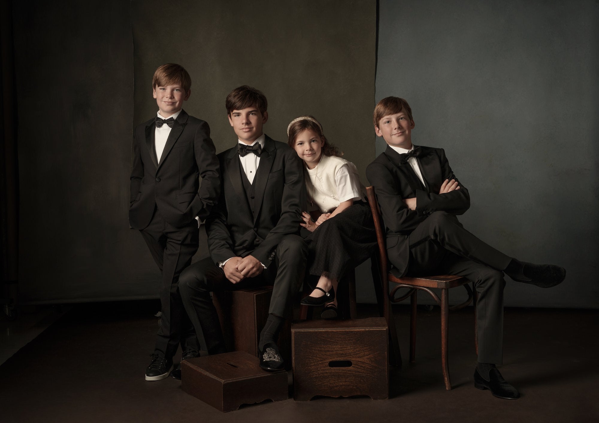 Formal studio group portrait of four kids in tuxes and a girl in a white top and skirt, seated and standing on apple boxes.