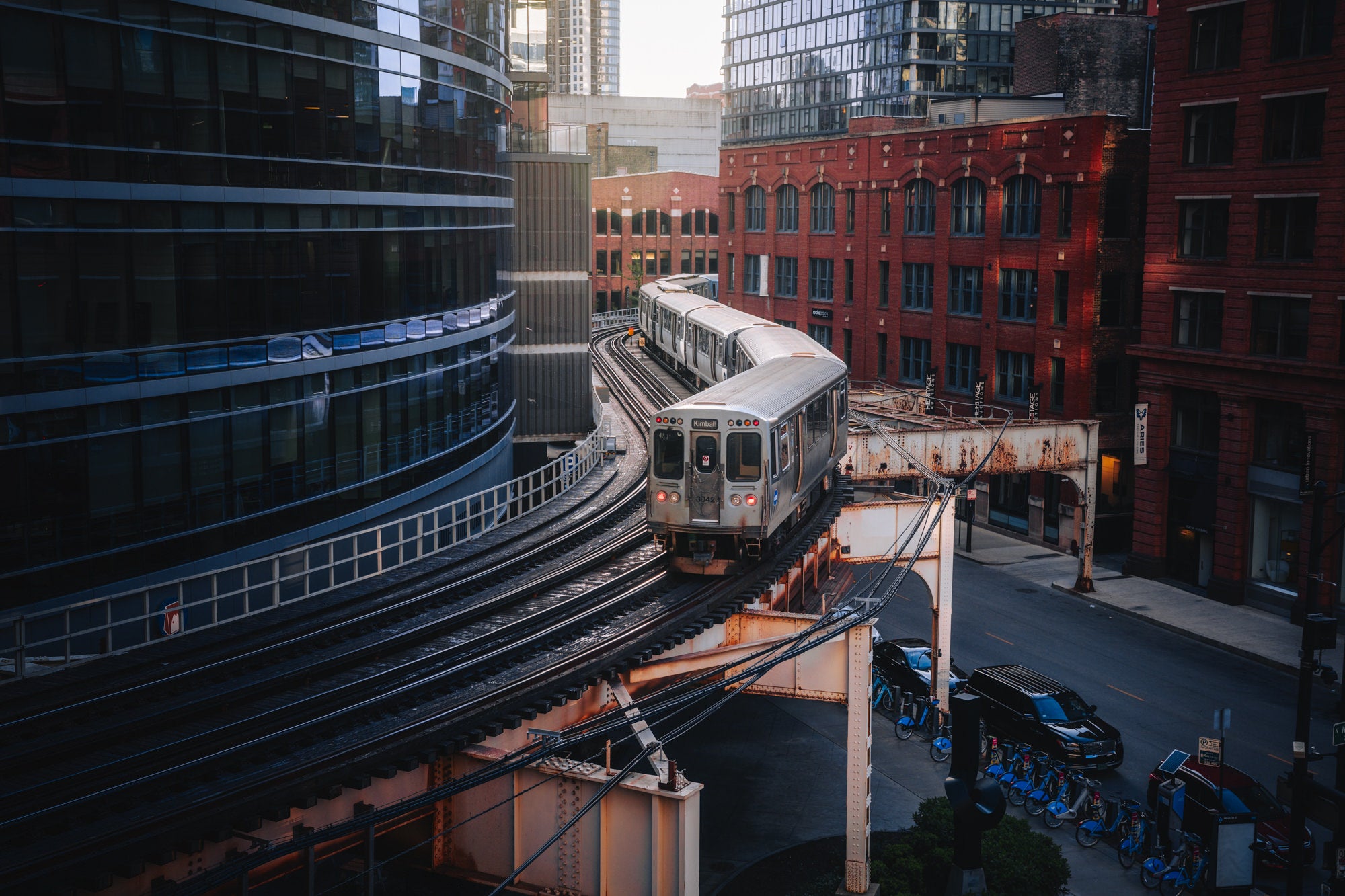 Chicago &lsquo;L&rsquo; train navigating curved elevated tracks among red-brick and glass buildings, urban transit image by Paul Clark.